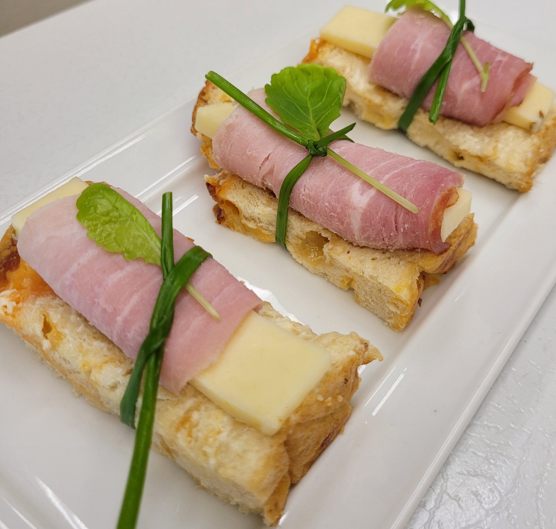 Prosciutto and brie canapés tied with fresh chives